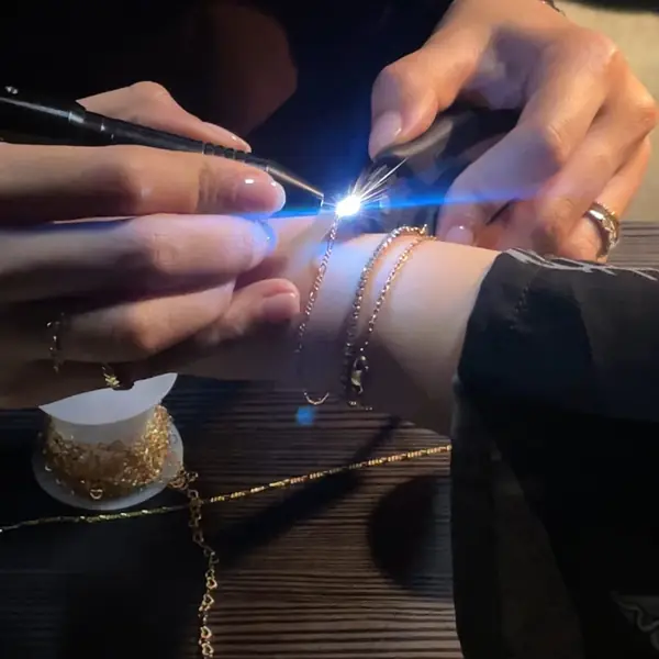 The welding pen flashes blue as it closes a gold chain on a client's wrist